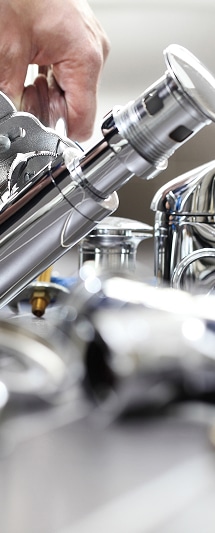 Plomberie : réparation et installation de robinetterie chrome. Main ajustant un mécanisme de vidage pop-up en chrome avec une pince, sur fond de robinetterie moderne. Installation de plomberie.