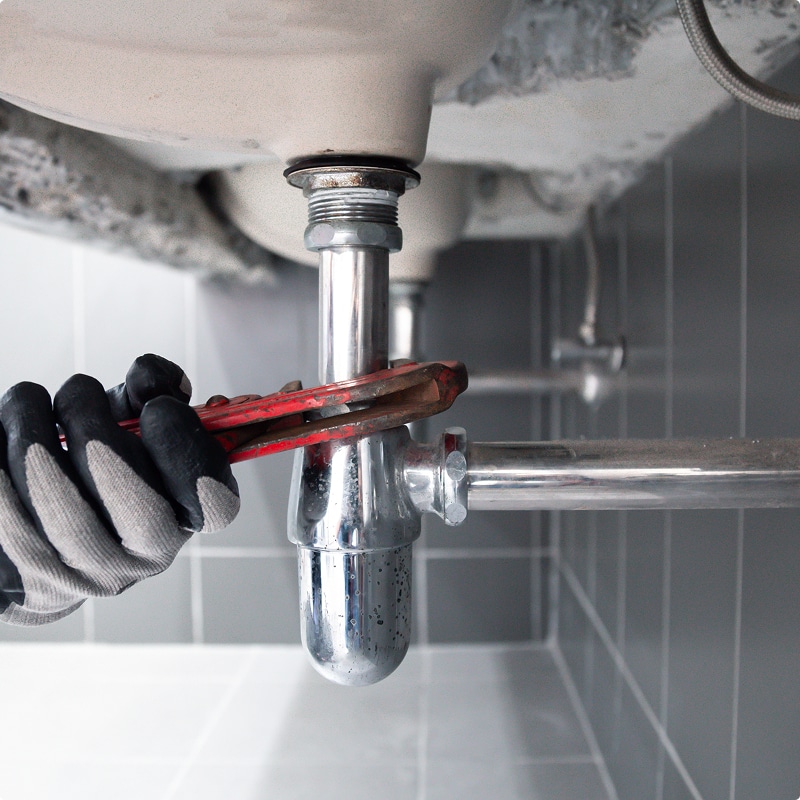 Plombier utilisant une clé pour ajuster le siphon chromé sous un évier. Maintenance et installation de tuyauterie.