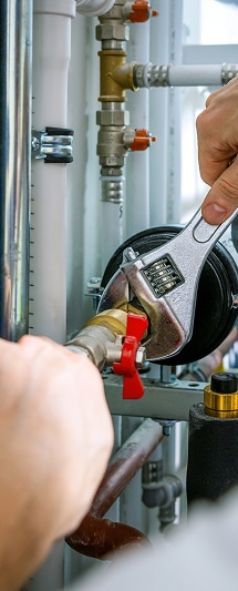 Plombier professionnel : réparation et entretien de chauffage Le Plombier utilise une clé à molette pour serrer un raccord en laiton et une valve rouge sur un système de chauffage et de tuyauterie moderne.